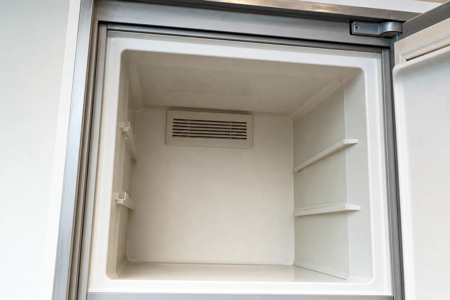 Empty freezer compartment liner with the cold-air vent and shelf supports, door standing open